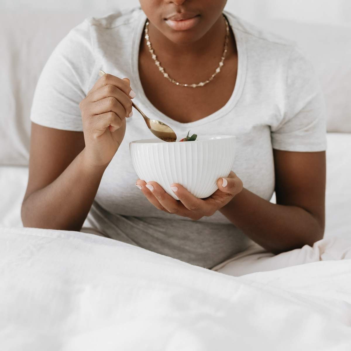 a woman sitting in bed eating breakfast out of a white bowl