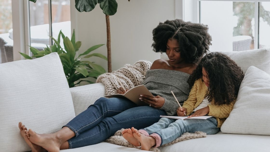 mother and daughter making lists together while cozied up on a white couch