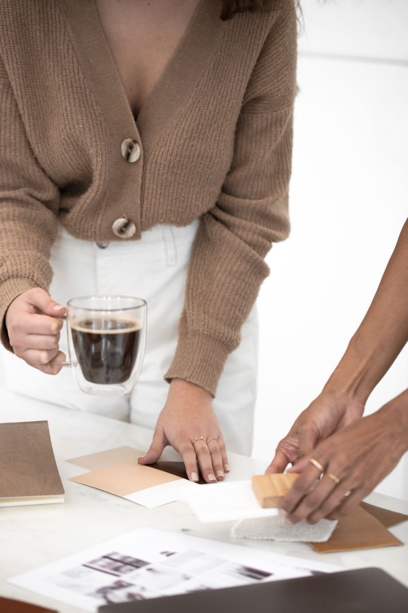Two women creating a design mood board at their office; one is holding paint chips, the other a block of wood