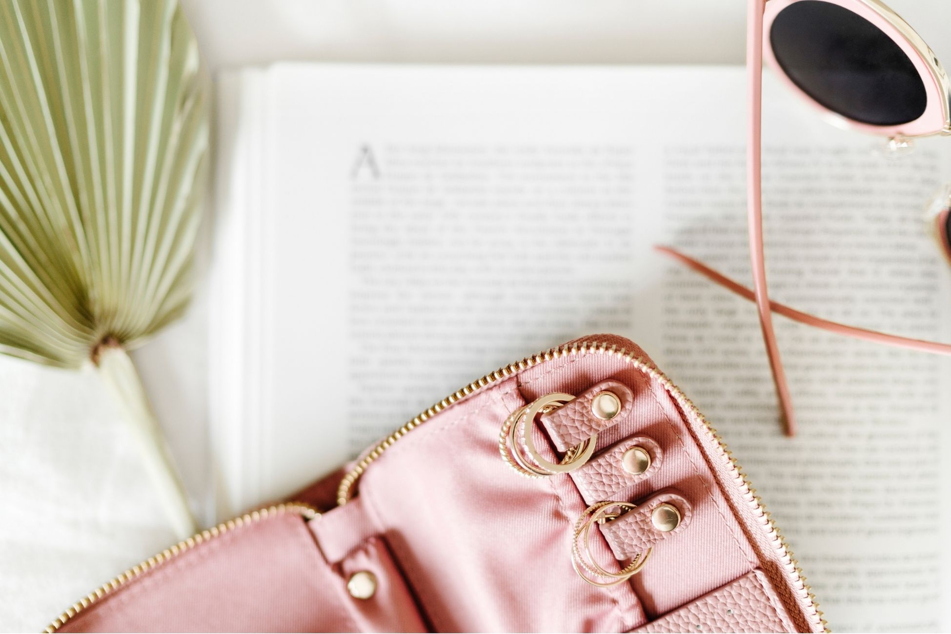 a pink zippered wallet, sun glasses and a journal collected on a table.