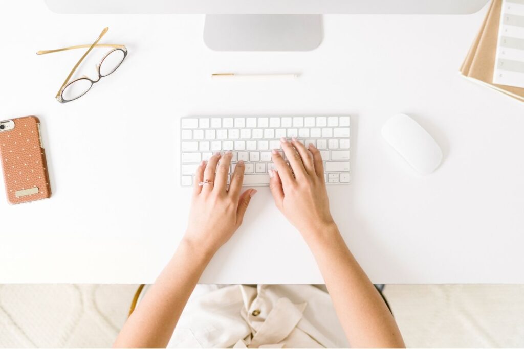 woman sitting at desk with hands on keys. Phone and glasses nearby.