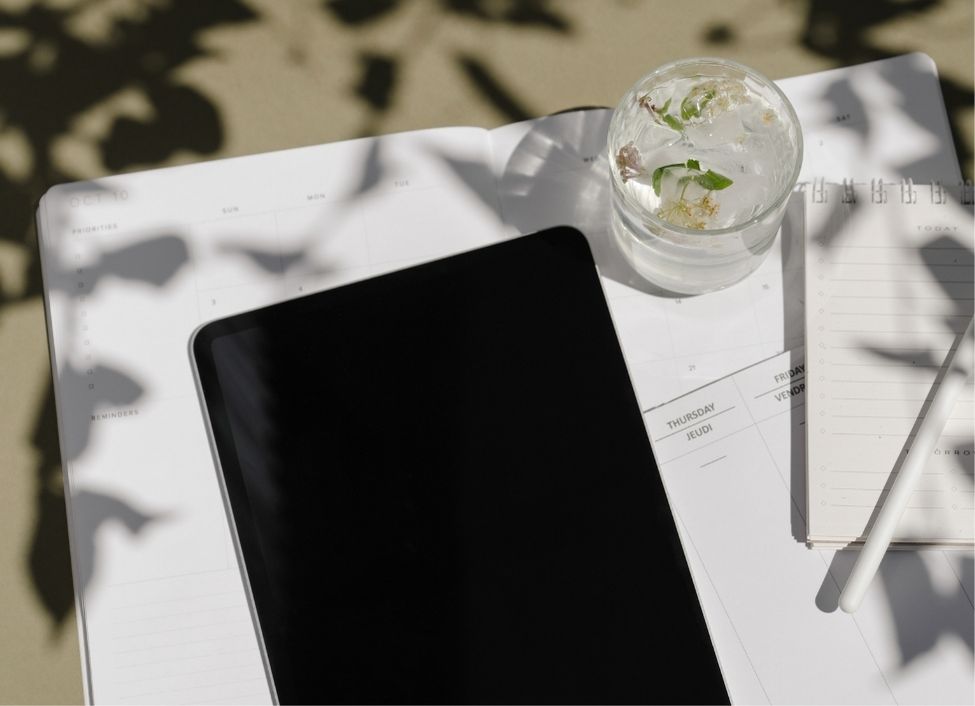A tablet and a calendar open and ready to take notes; a glass of water and pen are nearby
