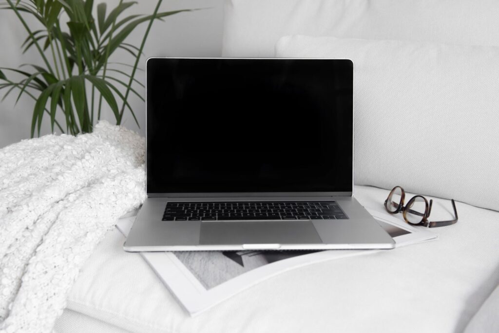 a laptop computer on a white couch, glasses are nearby
